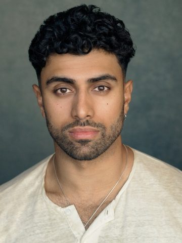 A headshot of a south Asian actor wearing a cream shirt, with dark brown hair