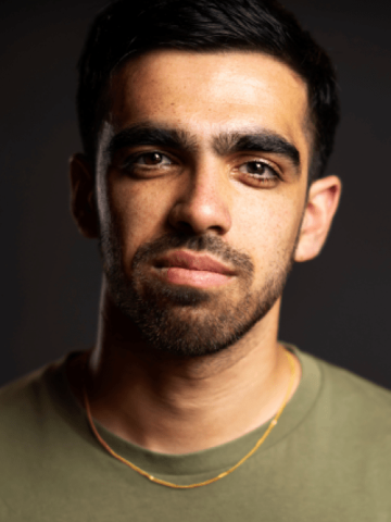 A headshot of an actor wearing a green t shirt, with dark brown hair